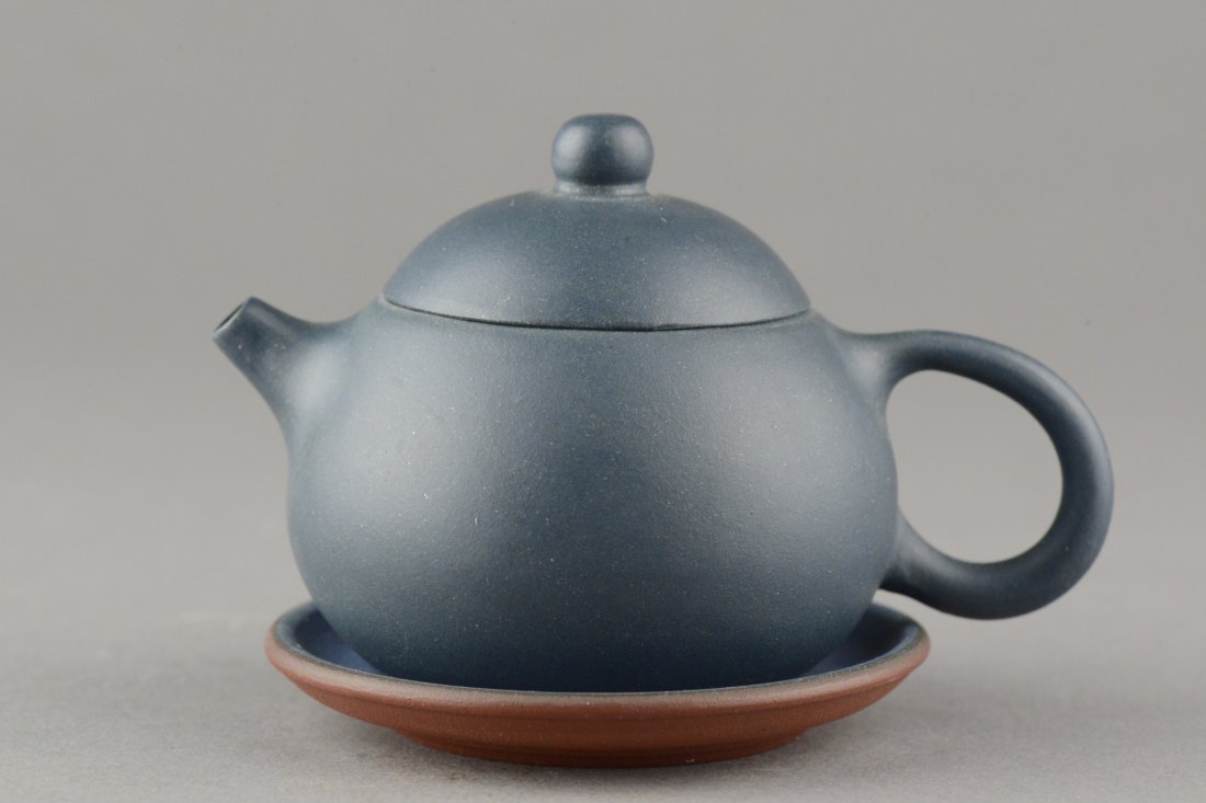 Delicate Chinese Zisha Teapot Zhou Lan Fang: Of globular form, the Zisha teapot is thinly potted and glazed in dark green. Bottom of lid and teapot marked artist name Zhou Lan Fang. Accompanied with blue saucer. H: 7 cm, W: 10 cm, 113 grams.