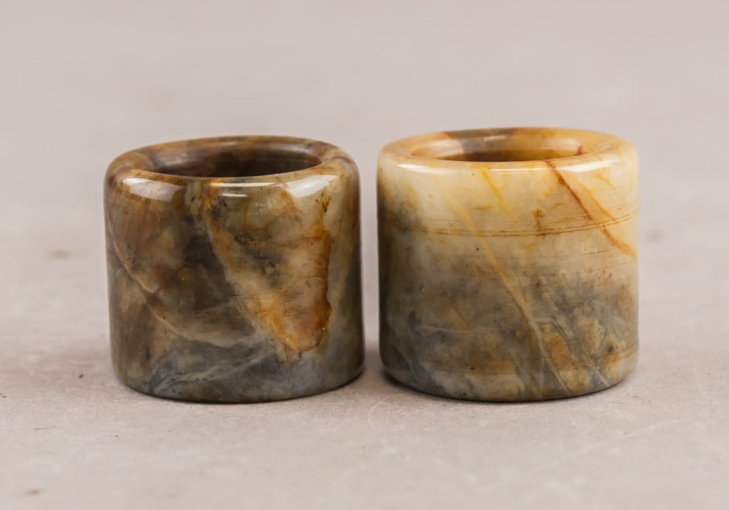 Chinese Old Jade Carved Archers Rings 2pc: Chinese Old Jade Carved Archers Rings, 2-piece set: This pair of traditional Chinese thumb rings is carved from natural jade, exhibiting a mix of earthy tones including brown, grey, and amber. Each ri
