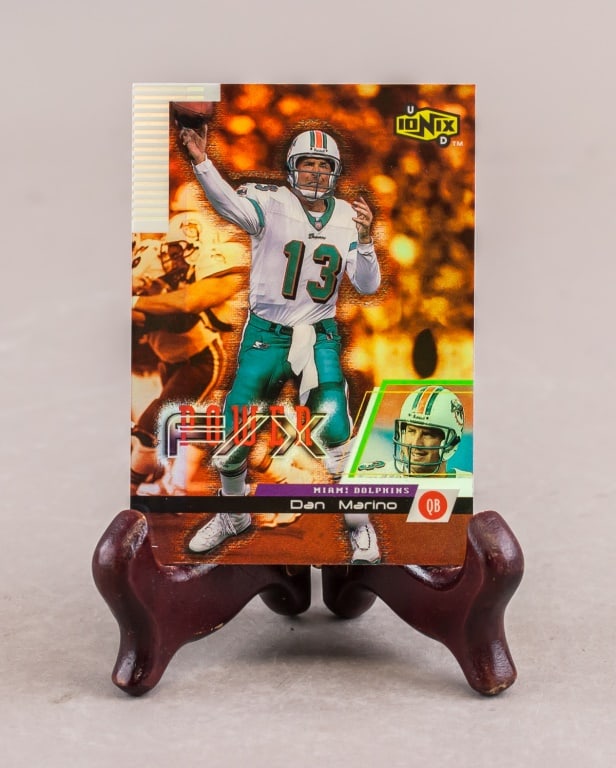 1999 Upper Deck NFL Dan Marino Card: This lot features a 1999 Upper Deck UD Ionix football card of Dan Marino, presented within a protective plastic sleeve. The front of the card displays an action shot of Marino in his Miami Dolphins un