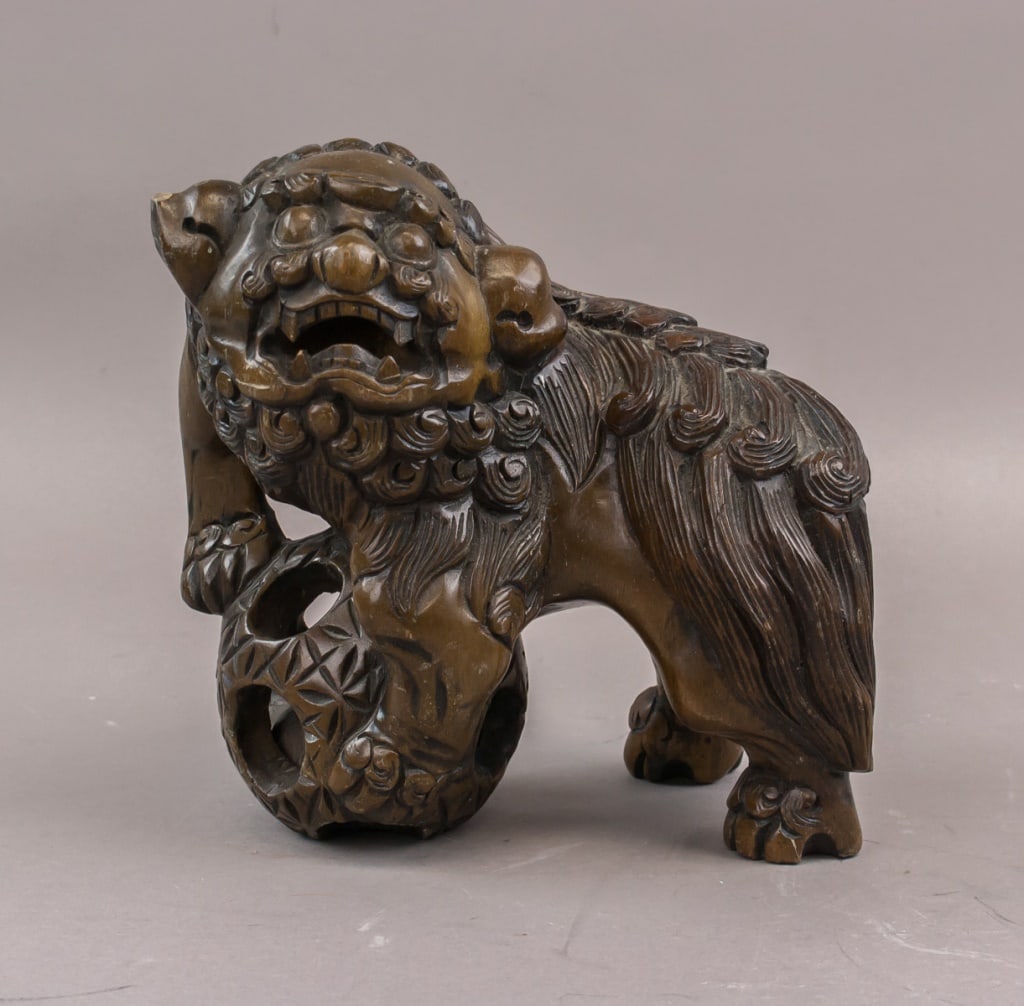 Chinese Wood Carved Foo Dogs: Pair of Chinese wood carved Foo Dogs, each depicted seated with stylized mane, expressive facial features, and muscular body. One figure rests a paw on a decorative ball. Carved details include fur te