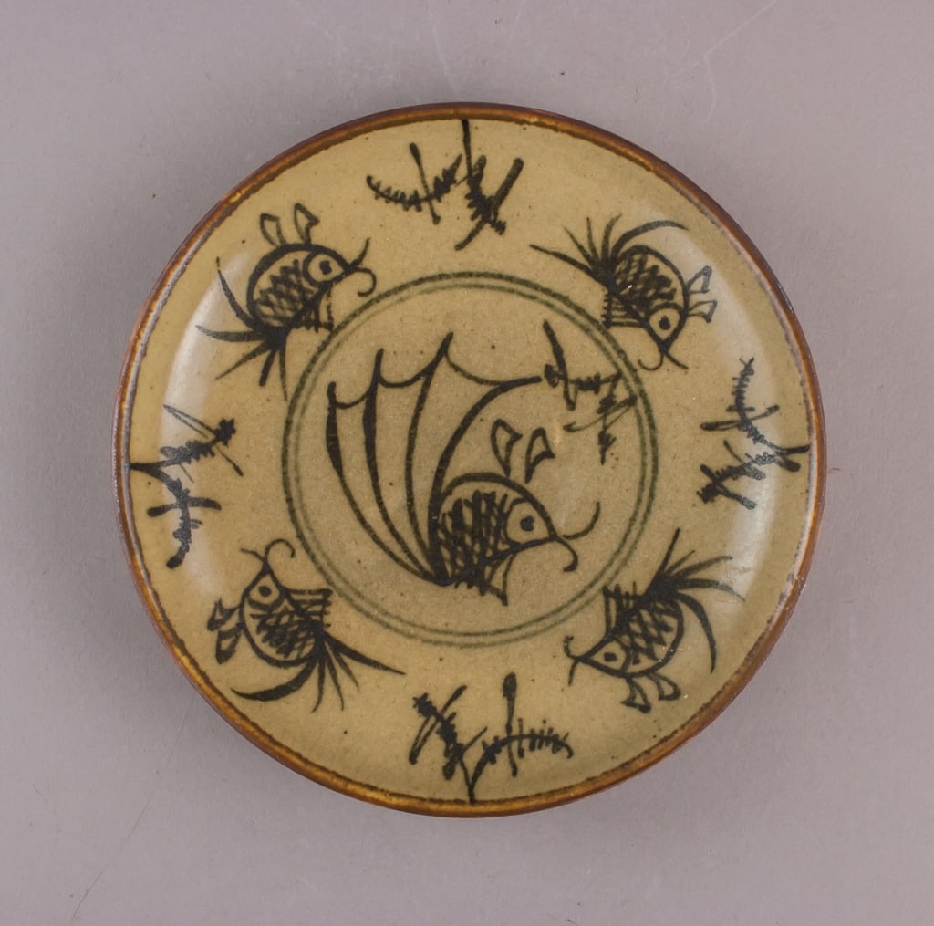 Vintage Thick Pottery Fish Plate: Thick pottery plate, vintage, with beige ground and black hand-painted design featuring central stylized fish surrounded by five smaller fish and abstract aquatic motifs. Brown rim with slight irregul
