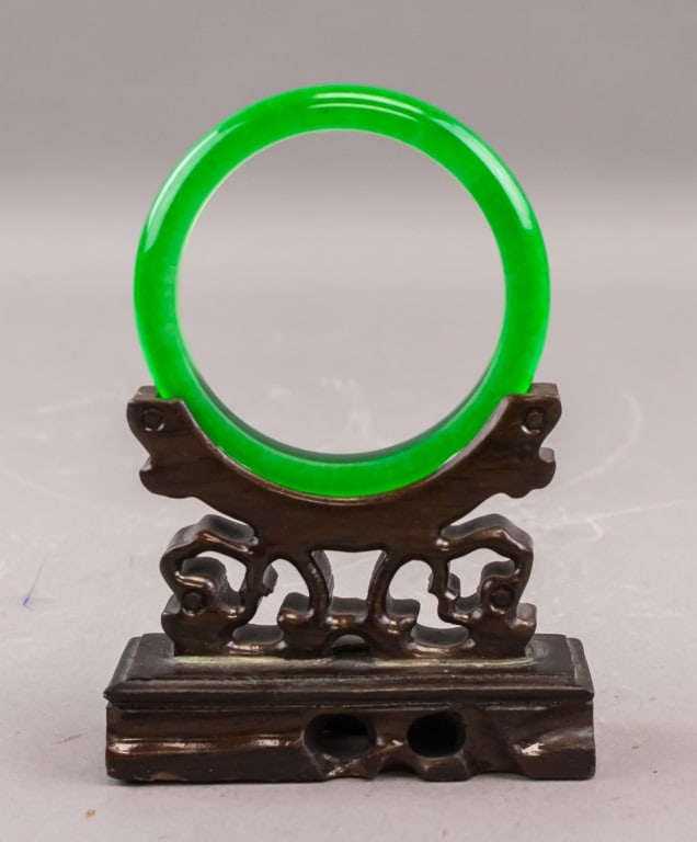 Chinese Green Jade Carved Bangle: A Chinese green jade bangle of circular form, well-polished and translucent with an even bright green tone. The piece is presented on a carved wooden stand (not included). Inner: 5.5 cm, Outer: 7.5 cm