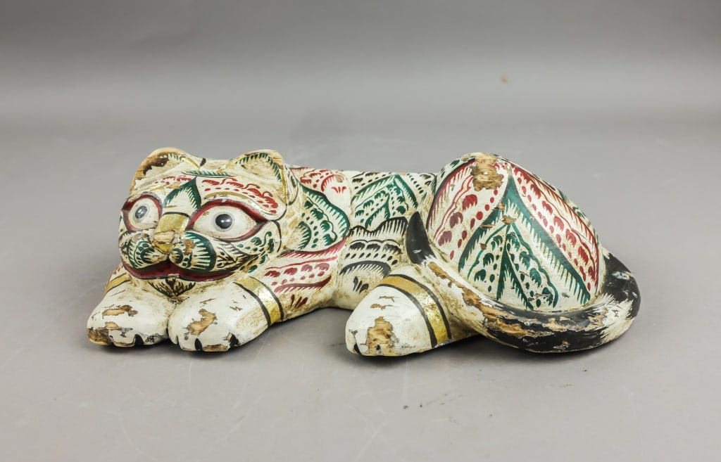 Vintage Indonesian Wooden Tiger Sculpture: A painted wooden tiger sculpture carved in a reclining pose, decorated with polychrome surface patterns in red, green, black, and gold over a white ground. The figure shows stylised facial features, i
