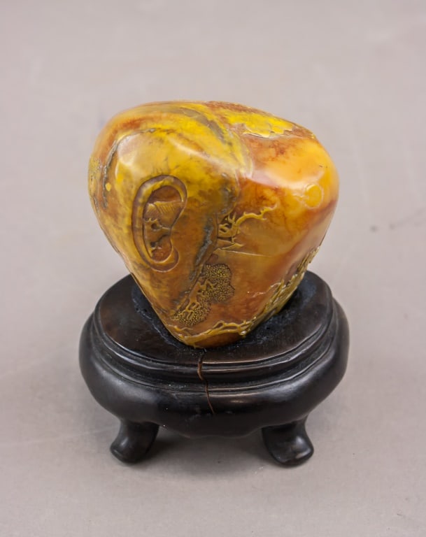 Chinese Fine Shoushan Stone Boulder w/ Stand: A Chinese Shoushan stone boulder carved in relief with a human ear and additional foliate motifs, the material showing natural yellow, orange, and brown tonal variation. The piece is offered with a fi