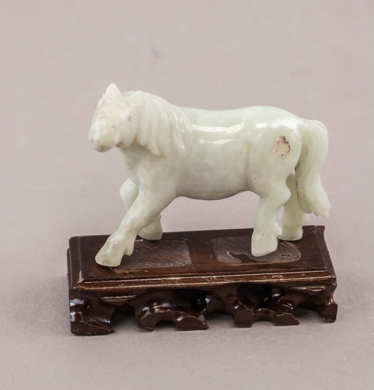 Chinese White Jade Carved Horse w/ Stand: A Chinese white jade horse carved in a walking stance with one foreleg raised and the head turned slightly, the stone of pale even tone with smooth polished surfaces. The figure is offered together wi