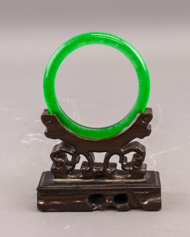 Chinese Green Jade Carved Bangle: A Chinese green jade bangle of circular form, well-polished and translucent with an even bright green tone. The piece is presented on a carved wooden stand (not included). Inner: 6 cm, Outer: 7.5 cm, 