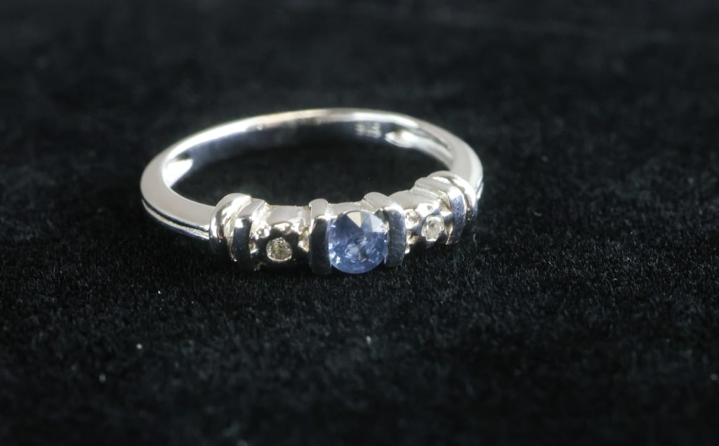 0.15ct Silver Blue Sapphire Ring w/Jewel Appraisal: 0.15ct round-cut natural blue sapphire ring claw-set in 925 sterling silver with cubic zirconia accents, the mounting weighing 2.11g and sized 6½, accompanied by a 2025 Jewel Scan appraisal det