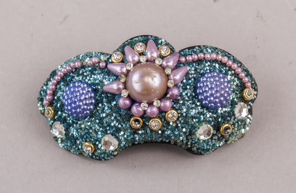 Vintage French Gemstone Hairpin: A vintage French hairpin decorated with a central pink cabochon surrounded by purple beads and rhinestones, set on a teal glittered ground with additional blue domed beads and pink pearl accents. H: 6