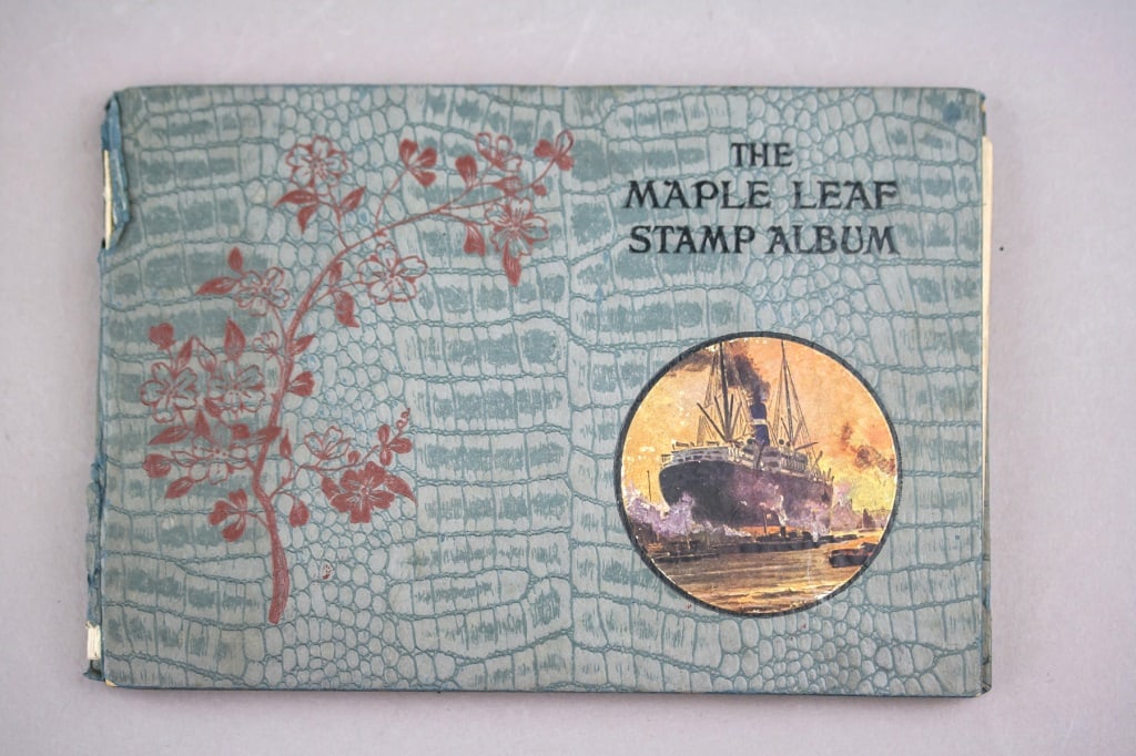 1922 Maple Leaf Stamp Album World Collection: A 1922 Maple Leaf Stamp Album containing a world collection. The album features its original textured cover with decorative motifs and houses an assortment of mounted stamps from various countries,