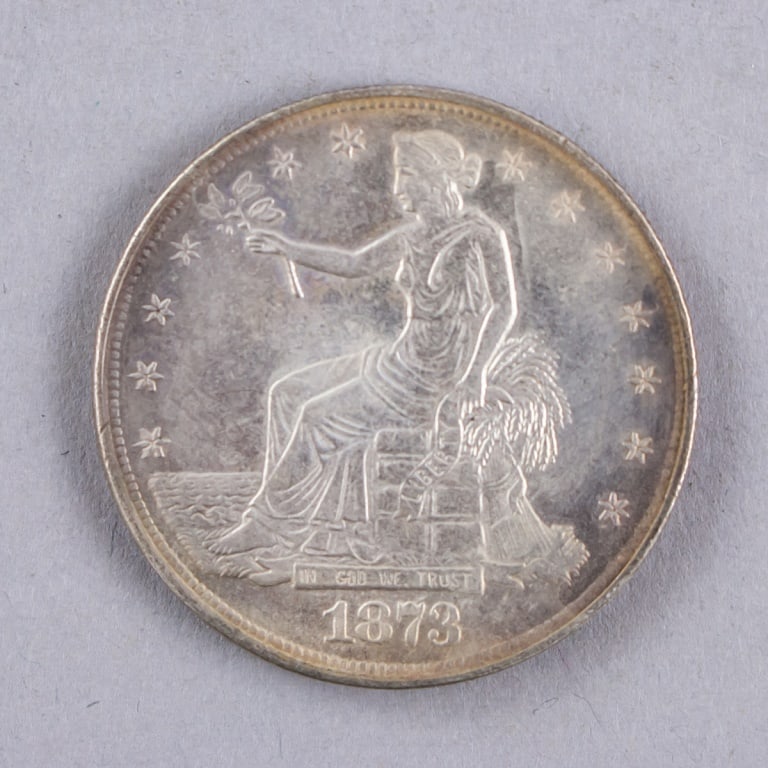1873 American Trade Dollar Coin: 1873 American Trade Dollar coin showing Liberty seated with olive branch and wheat sheaf above In God We Trust and the 1873 date, the reverse with eagle and denomination, the piece exhibiting circulat