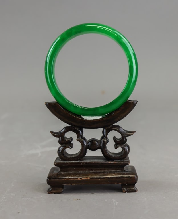 Chinese Green Jadeite Carved Bangle: Chinese green jadeite bangle of circular form, carved and polished to a smooth uniform profile with rich translucent green coloration and natural tonal variation. Wood stand not included. Inner: 5.5