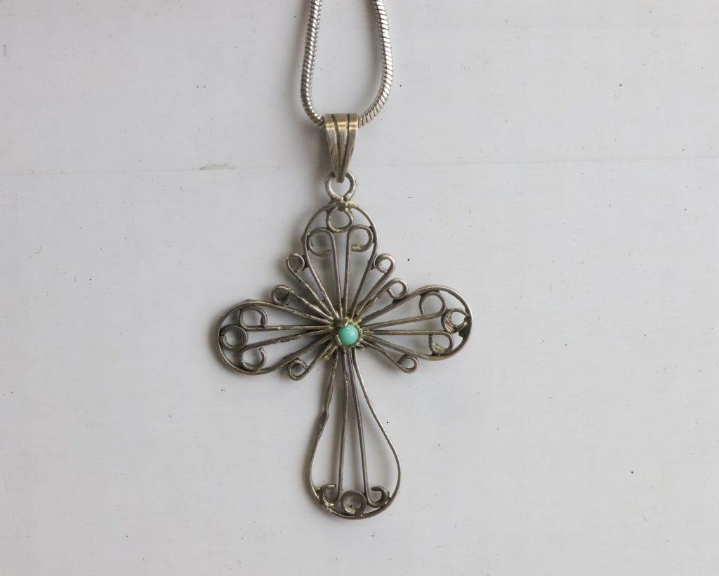 Vintage Filigree Silver-plated Cross Necklace: Vintage silver-plated filigree cross necklace featuring an openwork wire-scroll cross centred with a small turquoise-coloured cabochon, suspended from a smooth snake-style chain, the piece showing