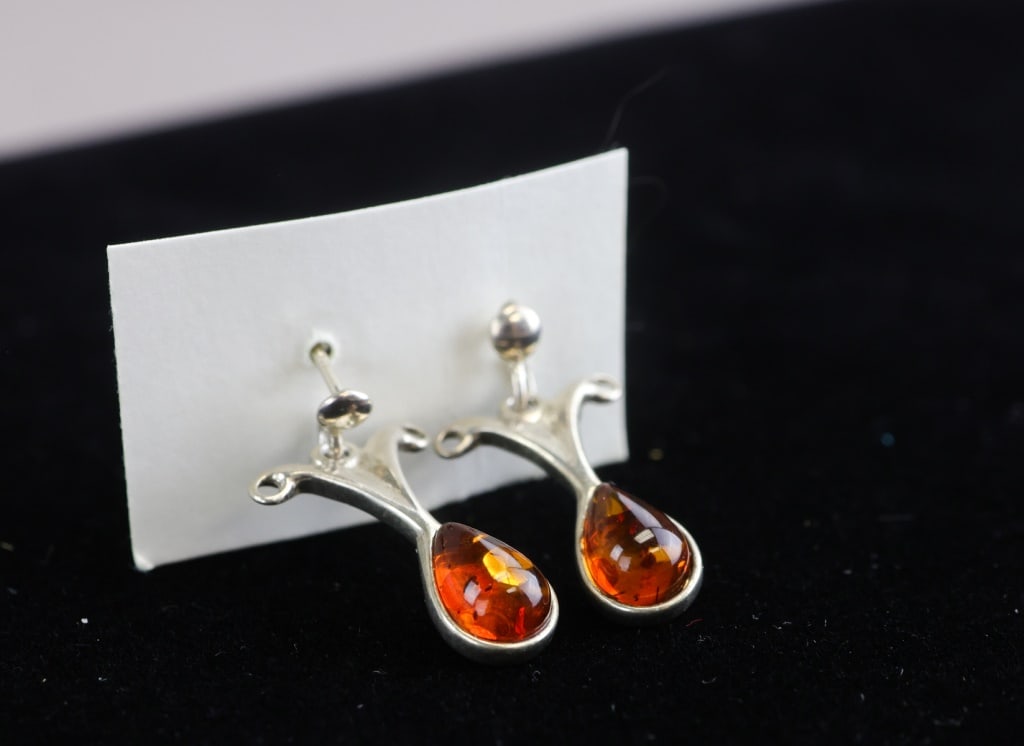 Vintage Sterling Silver Amber Earrings 2pc: Vintage sterling silver amber earrings, two pieces, each set with a teardrop-shaped polished amber cabochon in an ornate silver mount with curved decorative detailing, the pair showing warm