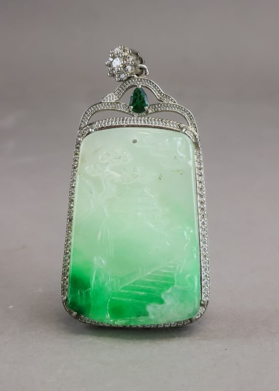 Chinese Light Green Jade Plaque Pendant: Chinese light green jade plaque pendant featuring a carved scene in mottled pale green and white jade, framed within a border of small clear stones and surmounted by an ornate mount set with a