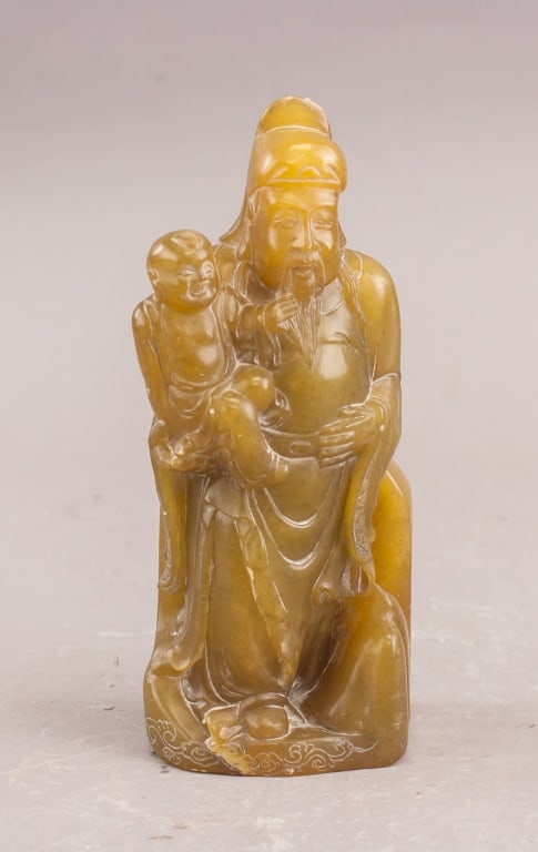 Chinese Shoushan Stone Carved Sculpture: Chinese Shoushan Stone Carved Sculpture. Carved from warm-toned Shoushan stone, this figure depicts a robed adult holding a child in a seated posture. The stone exhibits smooth polish with natural var