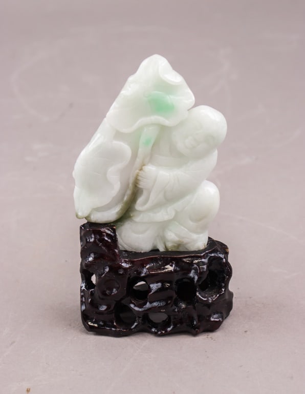 Chinese Green & White Jadeite Buddha w/ Wood Stand: A Chinese green and white jadeite carving depicting a seated Buddha figure, showing mottled pale and deeper green tones with smooth polished surfaces and defined carved details, presented on a fitted 