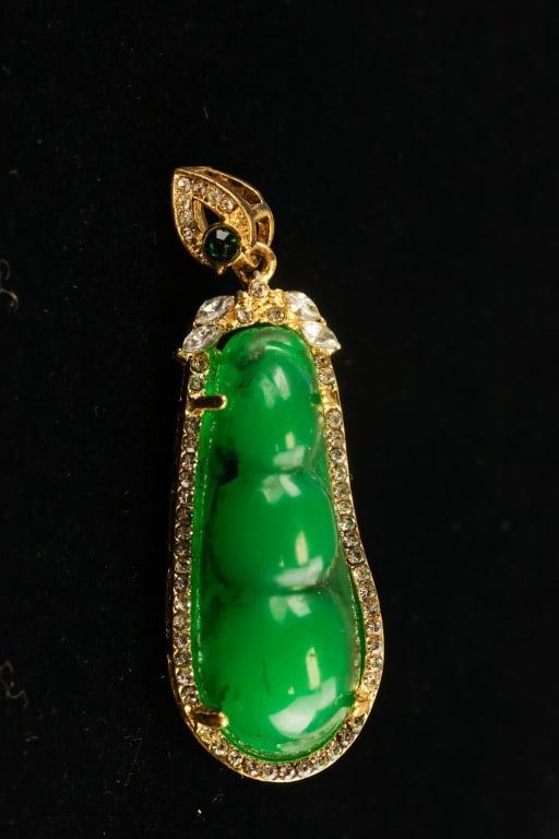 Chinese Peapod Green Hardstone Pendant: Chinese peapod green hardstone pendant featuring a bright polished three-lobed green hardstone carving set within a gold-plated frame accented by small clear stones, surmounted by a leaf-form mount
