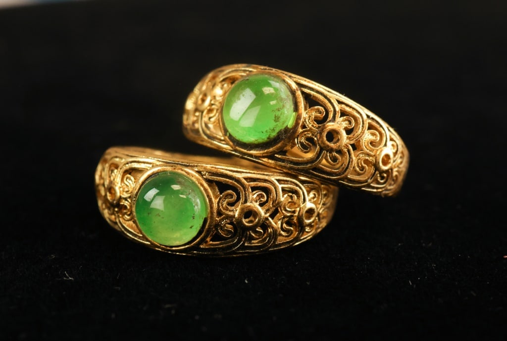 Chinese Gold-plated & Hardstone Rings 2pc: Chinese gold-plated and hardstone rings, two pieces, each set with a round polished green hardstone cabochon in ornate openwork mounts featuring scrolling and circular motifs, the pair showing bright 