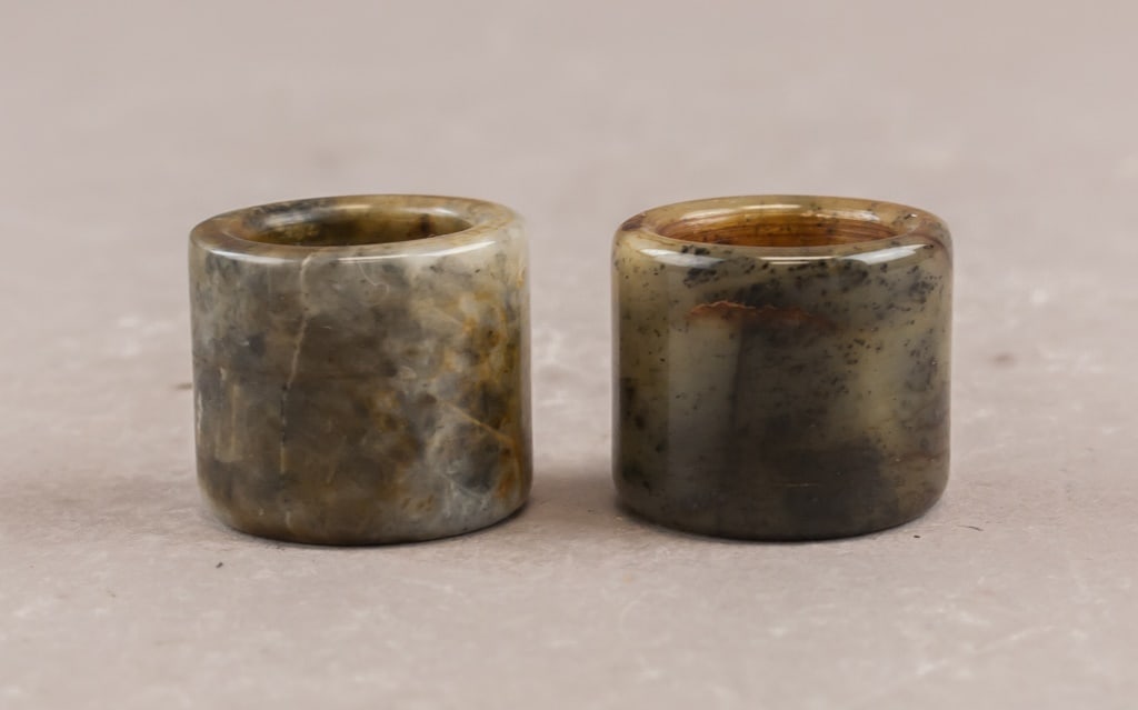 Chinese Old Jade Carved Archers Rings 2pc: Each cylindrical ring is crafted from mottled green and brown jade with natural inclusions and a polished finish. Inner: 2 cm, Outer: 3 cm, 68g (2)