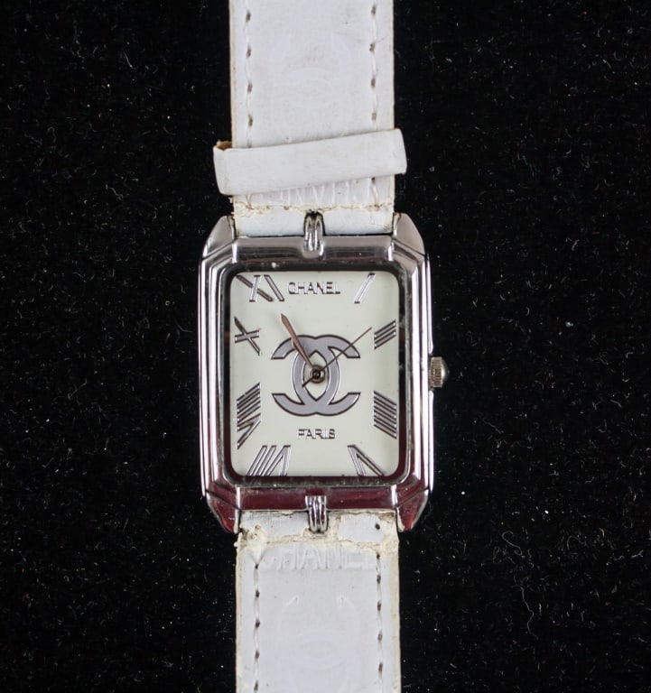 Vintage CHANEL Stainless Steel Watch: CHANEL wristwatch with rectangular white dial featuring silver Roman numerals, silver hour and minute hands, and ?CHANEL? and ?PARIS? printed at center. Case in stainless steel with white leather stra
