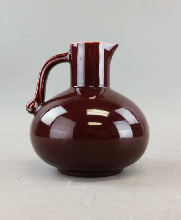 Chinese Reddish-brown Glazed Porcelain Pitcher: A rounded-body vessel rising to a narrow neck with a small pouring spout and an elegantly arched handle joining the shoulder and upper neck. The surface is finished in a deep, lustrous glaze that high