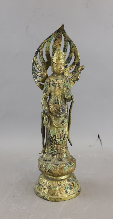 Antique Bronze Bodhisattva Guanyin Sculpture: A bronze Guanyin sculpture depicting the bodhisattva standing on a lotus pedestal, robed in flowing drapery and framed by an ornate flame-shaped mandorla with pierced detailing, the surface showing da