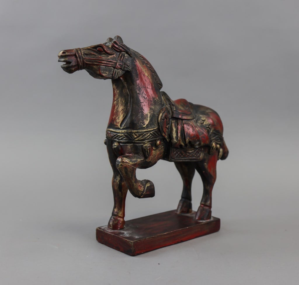 Vintage Red Wood Horse Sculpture: A red wood horse sculpture carved in a dark reddish-brown finish with gold accents, shown standing on a rectangular base with one foreleg raised, the body detailed with a patterned saddle and decorati
