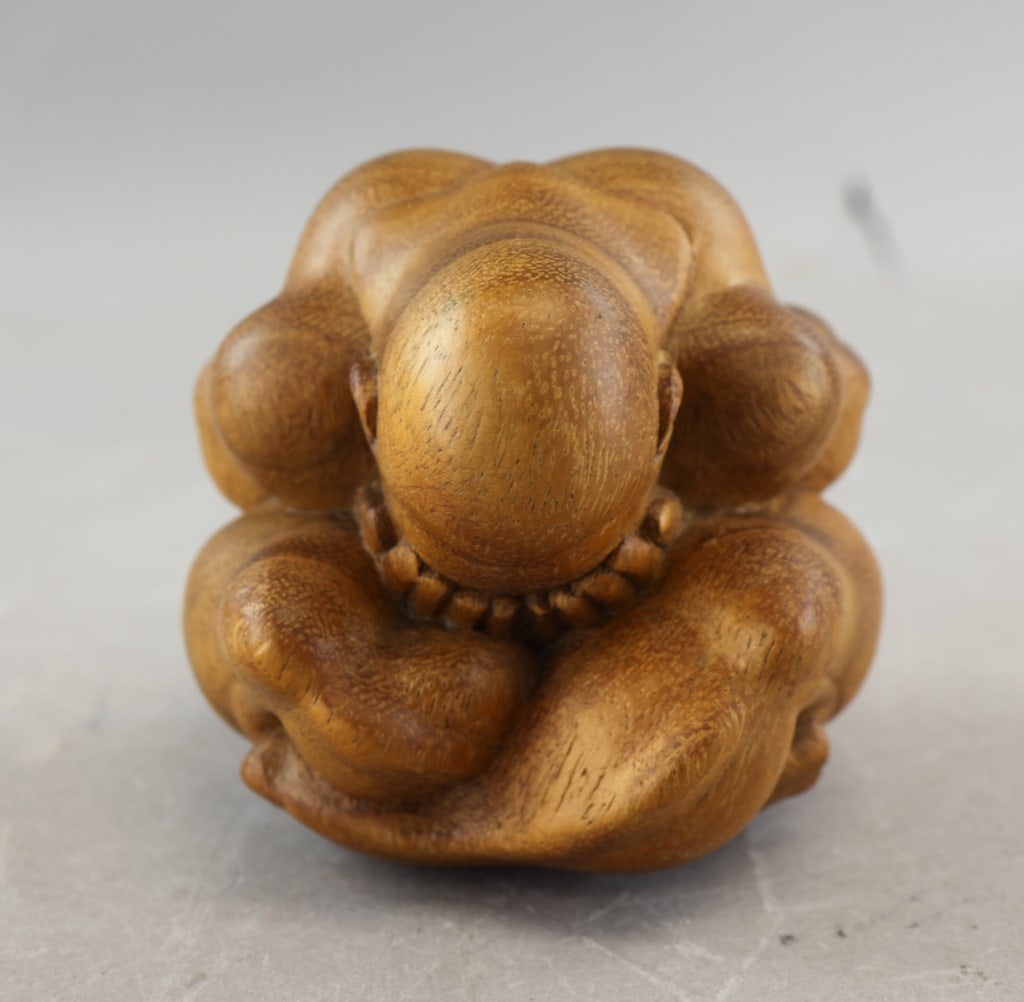 Japanese Wooden Seated Buddha Figure: A small wooden seated Buddha figure carved from a single piece of timber, the rounded form emphasizing the compact posture with folded arms and legs, the smooth surface highlighting the natural grain,