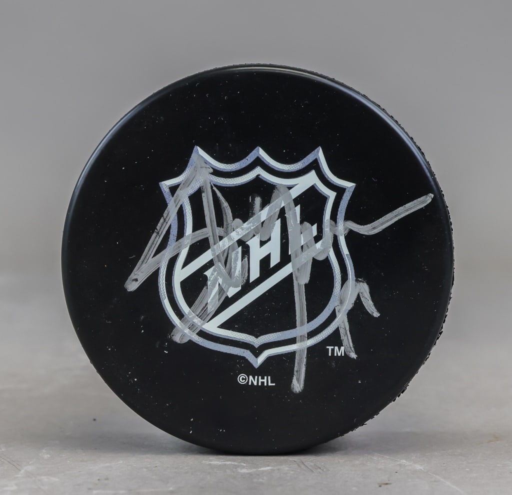 NHL Puck Signed Steve Yzerman: A black NHL-branded hockey puck bearing a silver-ink signature attributed to Steve Yzerman, presented as a single signed hockey collectible. H: 2.5 cm, Dia: 7.5 cm, 167g. *This lot has not been authen