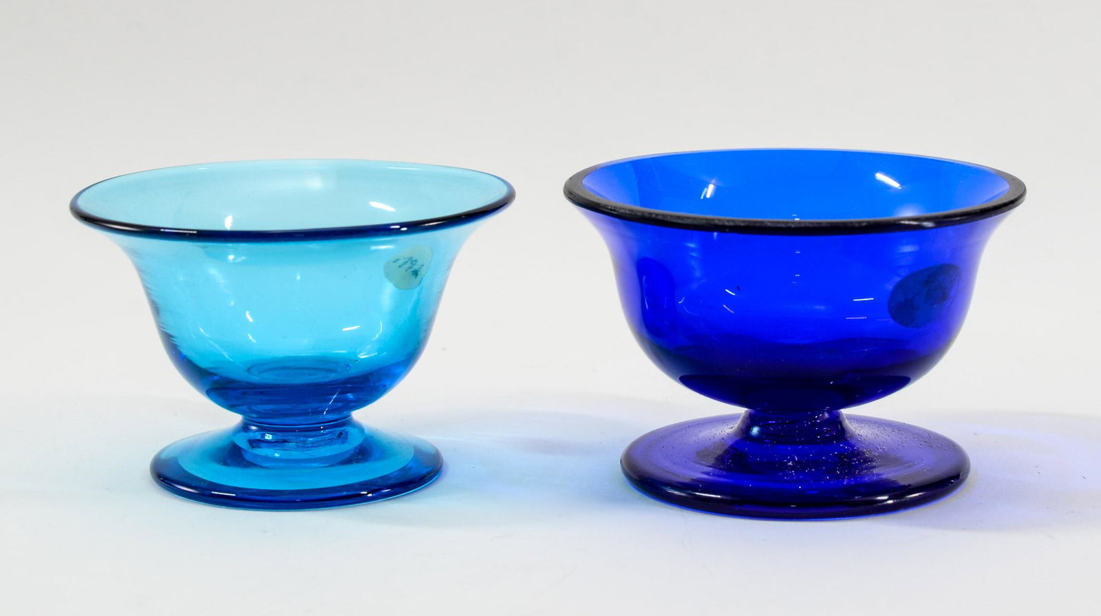 Two Blue Glass Pedestal Open Salts: Manner and style of Steuben, the celeste-type salt with a polished pontil (unmarked). The deeper blue piece without a pontil, but having a cut and polished rim. Measures 1 1/2" tall by 2 1/2" wide for