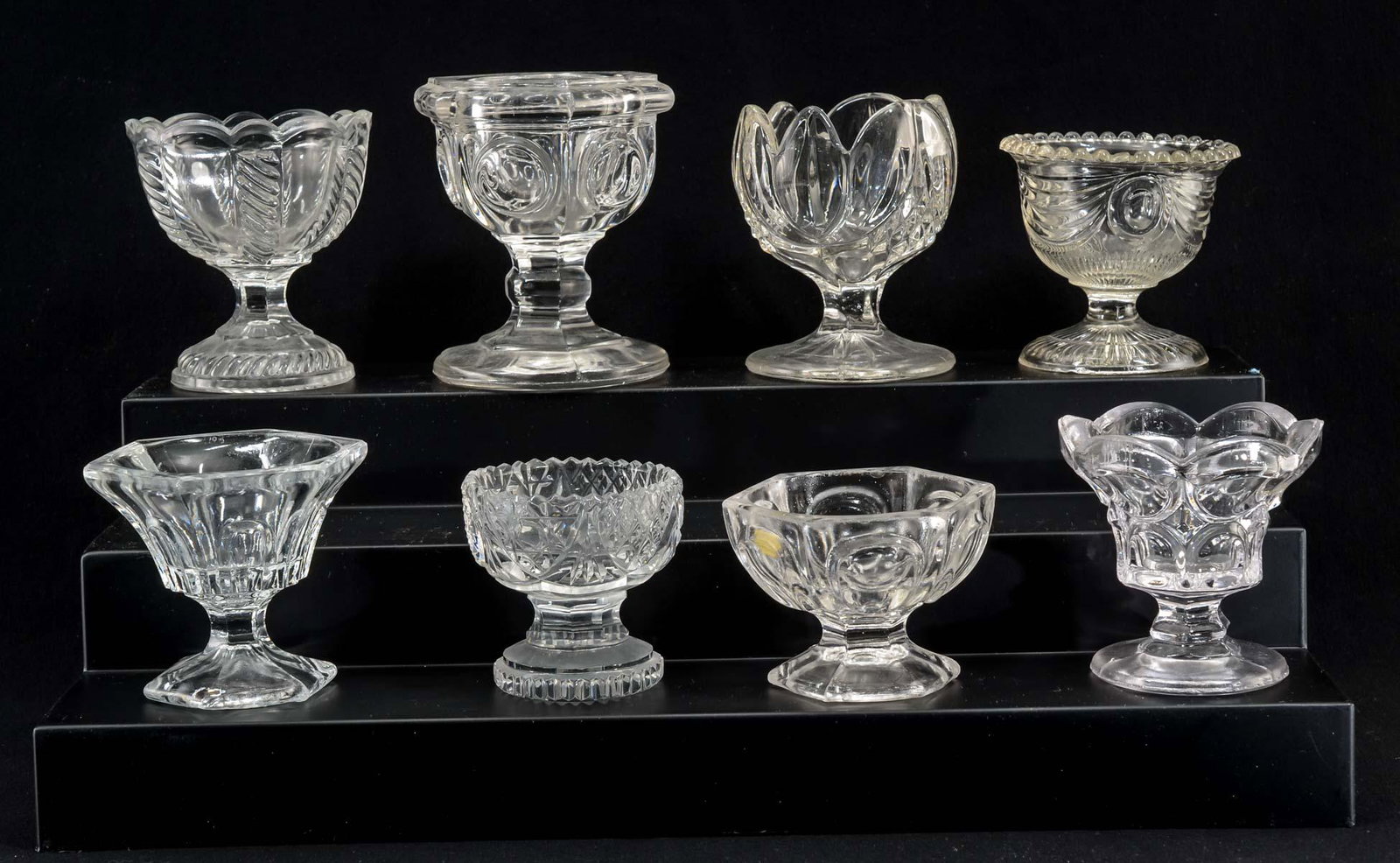 8 Pattern Glass Pedestal Salt Cellars: Includes Lincoln Drape, Twist, Tulip, press-cut, Thumbprint, and loop patterns. Size and Condition vary with fleabites, minor chips, shelf wear, but no major cracks, damage or repairs, Largest stands 