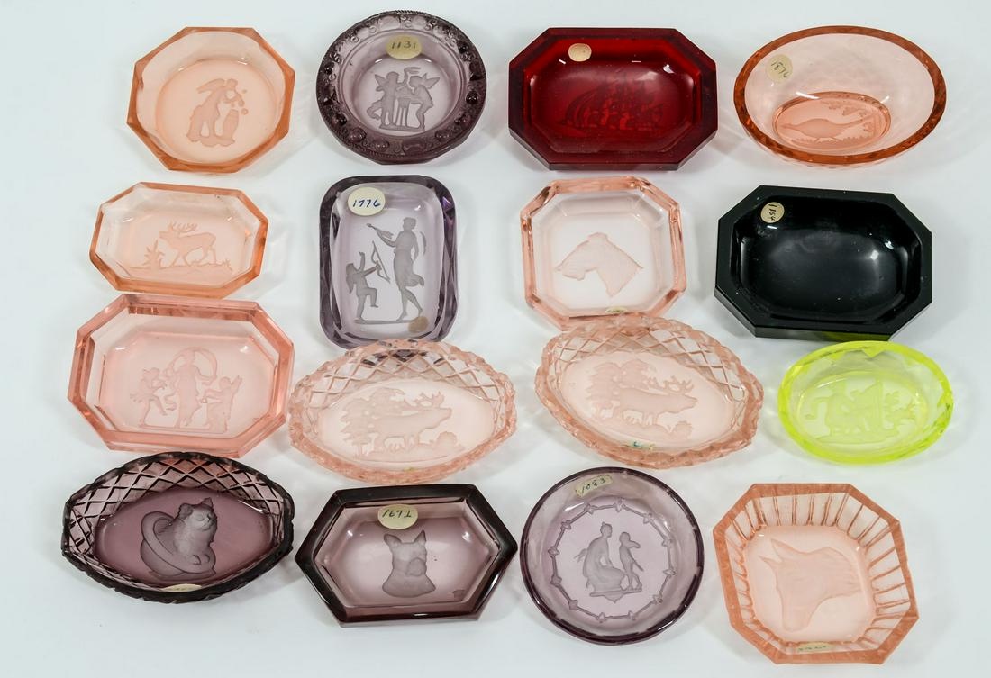 16 Colored Intaglio Glass Open Salts: Sixteen colored Intaglio cut glass open salts. Colors: Amethyst, ruby, pink, Vaseline, dark green. Subjects include: Pheasant, dog heads, Classical, cat head and ship. All appear to be in good conditi