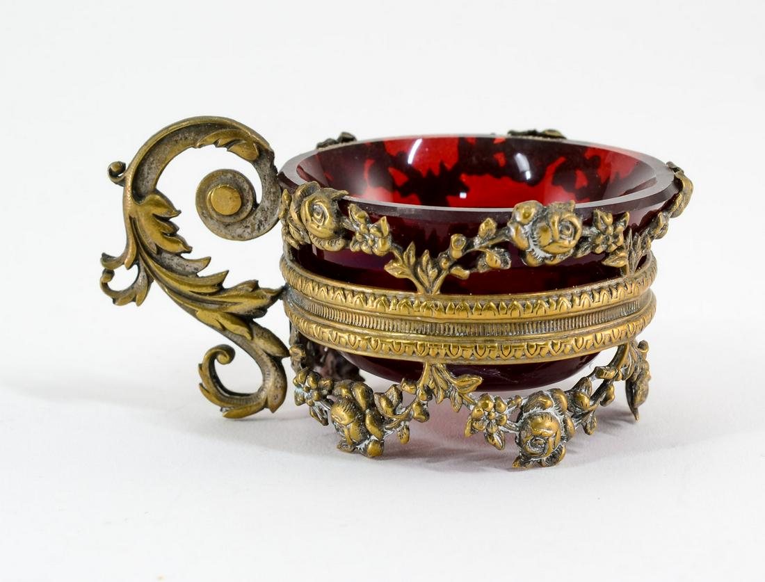 Ruby Glass Open Salt in Bronze Frame: Ruby glass salt in embossed floral swag bronze frame, having scrolling foliate handle. Unmarked. 1 1/4" diameter x 1 1/4" high. In excellent condition. Keywords: Salt Cellar, Salt Dip, Antique, French