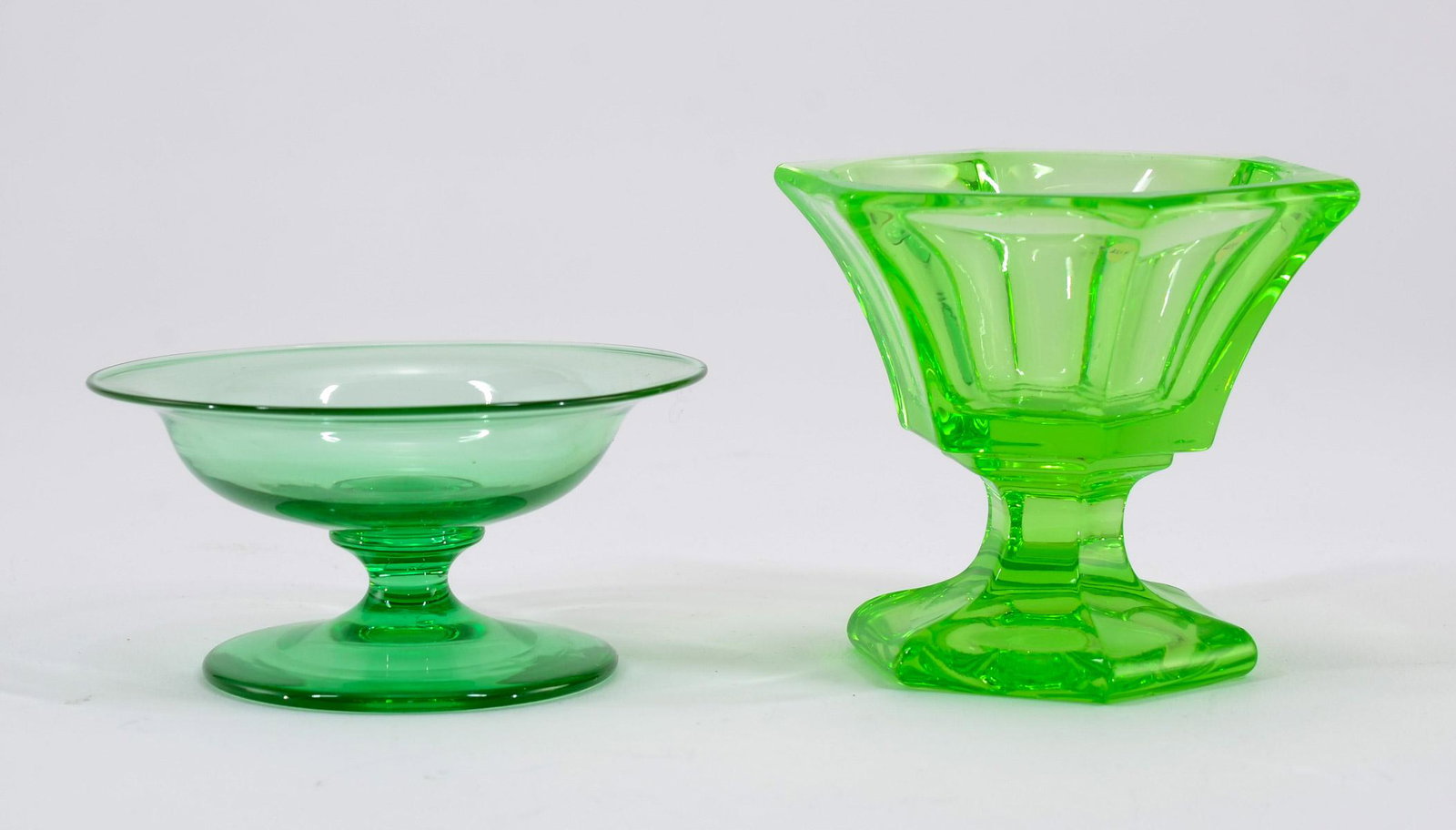 2 Vaseline Glass Pedestal Open Salts: Two green glass pedestal open salts. Including: Hexagonal bright apple green Flint EAPG Style and a hand blown Steuben Pomona Green Type, unsigned. Each with polished pontils. Keywords: Salt Cellar, S
