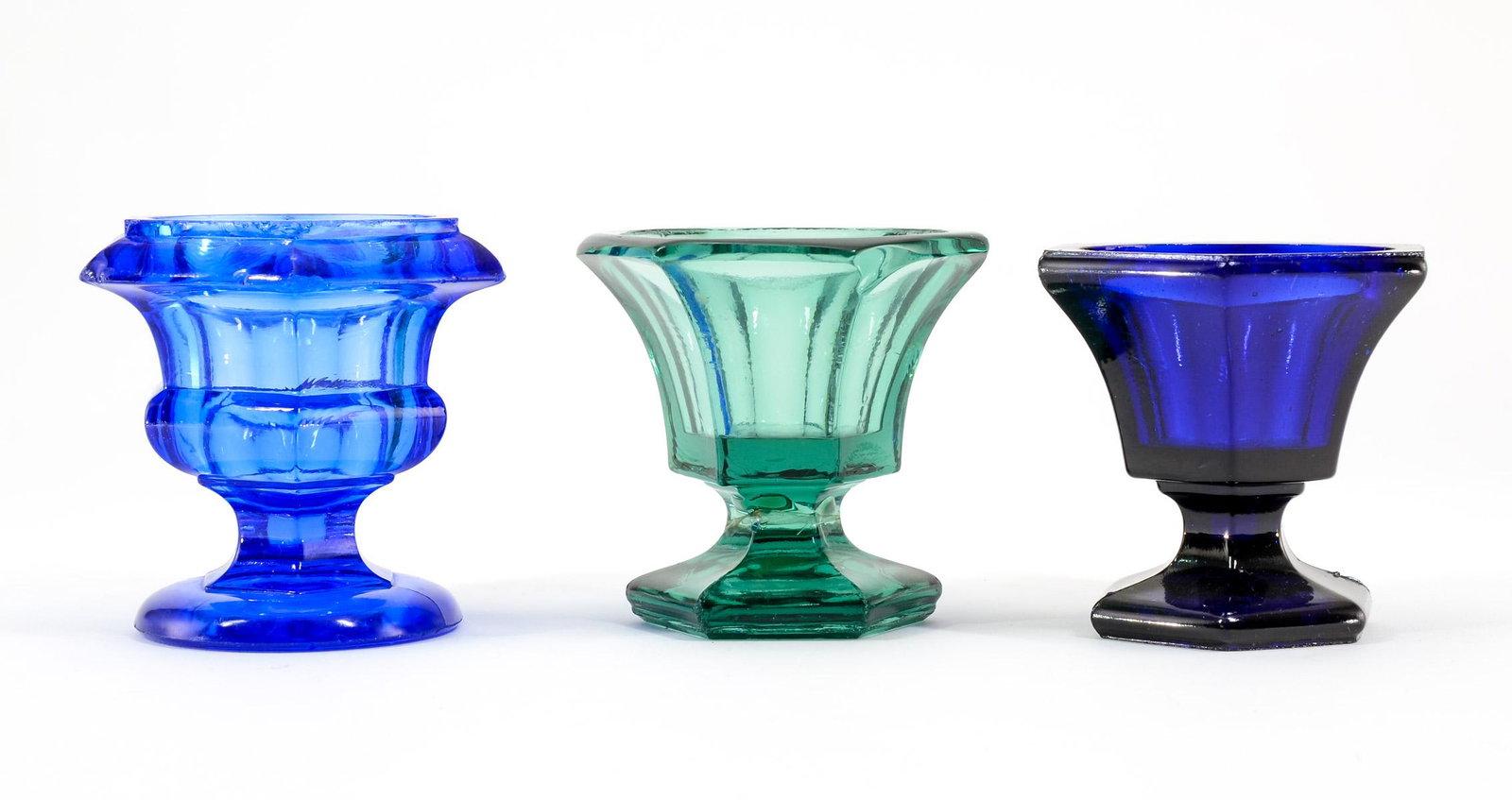 3 Early Colored Glass Pedestal Master Salts: Three early pressed colored glass hexagonal pedestal open master salts. Colors include: Emerald green, cobalt blue and royal blue. Royal blue has sizable chip in foot. Keywords: Salt Cellar, Salt Dip,