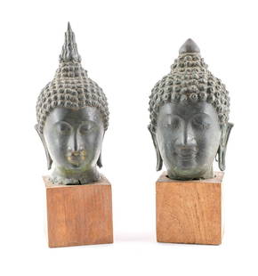 2 Thai Bronze Buddha Heads: Pair of two bronze Buddha heads on wooden bases. Thailand, ca. 19th century. In the Sukhothai style (14th century style). One has a flame halo atop the Buddha's node, while the other has a smooth