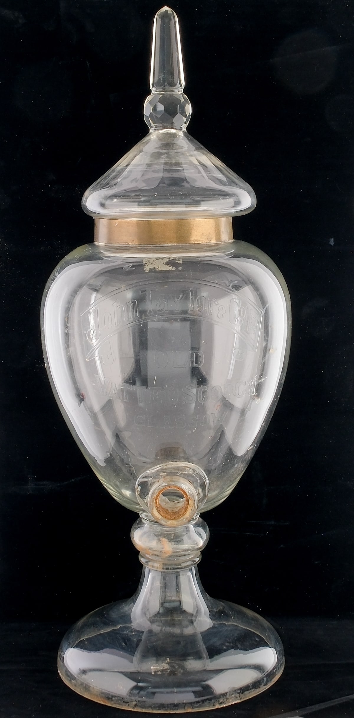 John Taylor & Co. Ltd Glass Scotch Dispenser: Grand old hand-blown glass scotch dispenser embossed with the words "John Taylor & Co. Ltd" across a banner and "Old Vatted Scotch - Glasgow" beneath. 19th Century. Missing its spigot and the rubber l