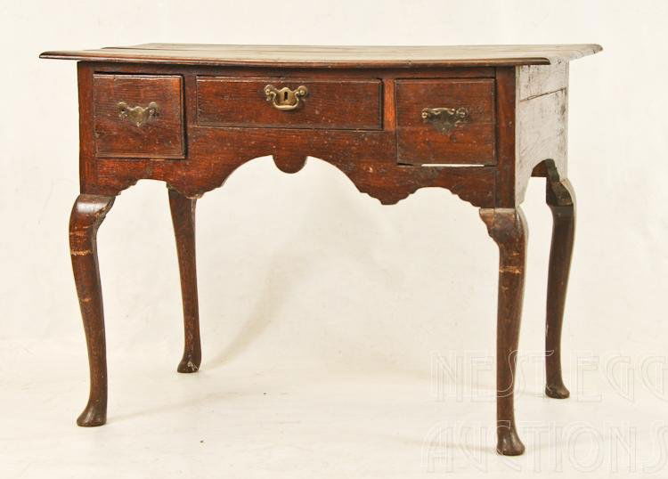 English Oak Lowboy: English George II lowboy or dressing table. Oak and oak as secondary wood. Three horizontal drawers with original brass batwing pulls (not original. One broken). Shaped apron. Cabriole legs terminatin