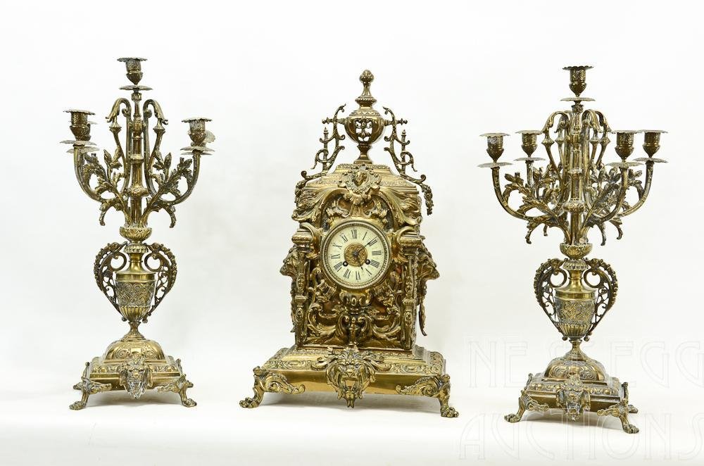 AD Mougin French Brass Figural Lions Head Clock Set: The Clock Being 22.5" Tall, and two garnitures each 23" Tall. Bobeches on the candelabra are loose, otherwise excellent condition. Early 20th Century.