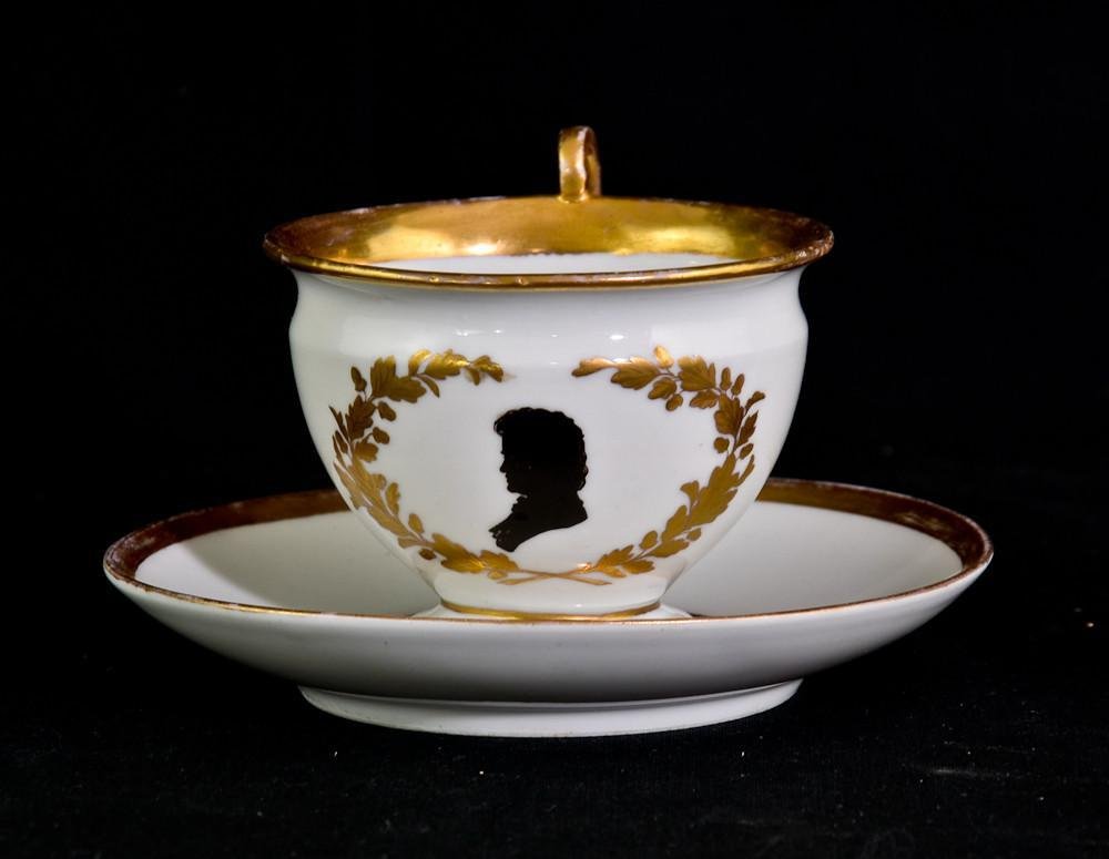 Marcolini Meissen porcelain Beethoven teacup: Marcolini Meissen cabinet tea cup and matching saucer. Blue crossed swords mark, circa 1815. Black with silhouette of Beethoven within gilt branches. Named on saucer 3.5" x 5.5"