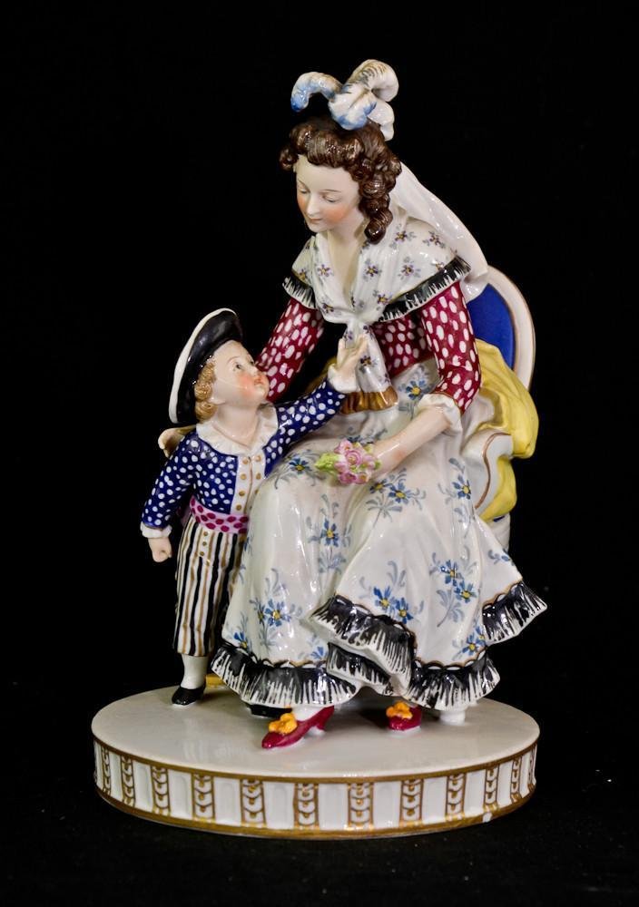 Ludwigsburg style porcelain figure of mother & child: Spurious blue crowned interlaced C mark, late 18th century. Mother wearing white dot red bodice, blue flowered skirt and plumes of feathers in her hair. The boy is in brimmed hat, white dot blue shirt