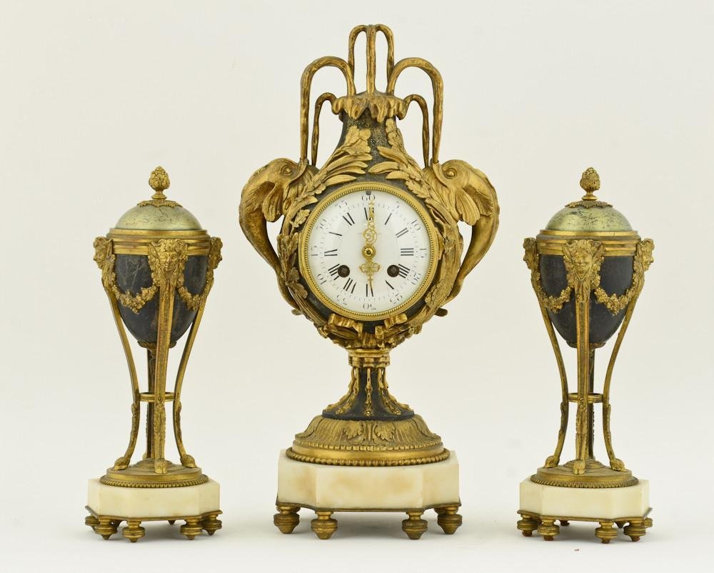 French Gilt Bronze & Marble Clock Set: Retailed by Tiffany & Co. Late 19th Century, Gilt Bronze Clock with mythological dolphins, and a pair of Garnitures with satyr decorations and flip candlesticks / finials. Some wear to case surfac