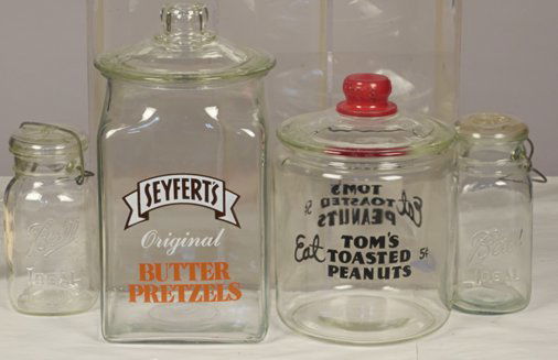 Lot Of 4 Glass Countertop Jars:: Lot Of 4 Glass Countertop Jars: 2 - Embossed Ball Ideal Mason Jars w/ Lids & Metal Handles - each approx. 8"h, 1 - Eat Tom's Toasted Peanuts 5 Cents Round Display Jar w/ Lid & "Tom's" embossed metal k