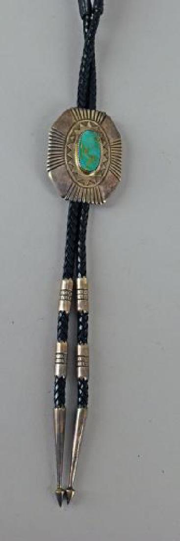 Milton Tsosie, Navajo Or Mary Tenorio, Zuni Bolo: Consisting Of A Green Turquoise Center Stone With Decorative Ray And Sun Design, With A Leather & Sterling Silver Worked Tips. The Bolo Measures 20 Inches Long On Each Side, The Center Piece Is 3 Inch