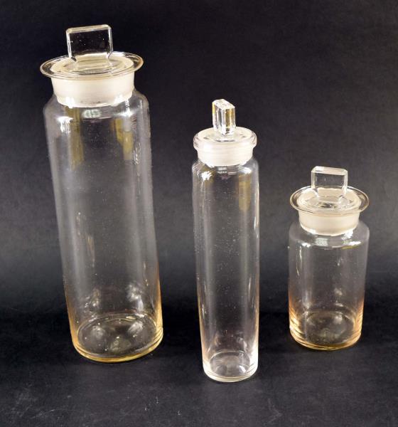 Three Apothecary Cylinder Glass Jars: Consisting Of Three Various Sizes Of Apothecary Jars With Frosted Rims And Tops. The Tallest Jar Measures 11.5" Tall And 3.25" Across, The Smallest Measures 6.5" Tall And 2.75" Across, The Middle Jar 