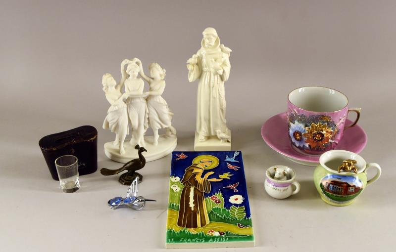 A Group Of Miscellaneous Items: Consisting Of A Hummel St Francis Figure, Missing Hand, A German Pink Lustre Coffee Cup And Saucer, Good Condition, A Bisque 3 Maiden Figure, Two Pigs In A Chamber Pot Souvenir Figures, A Brass Peacoc