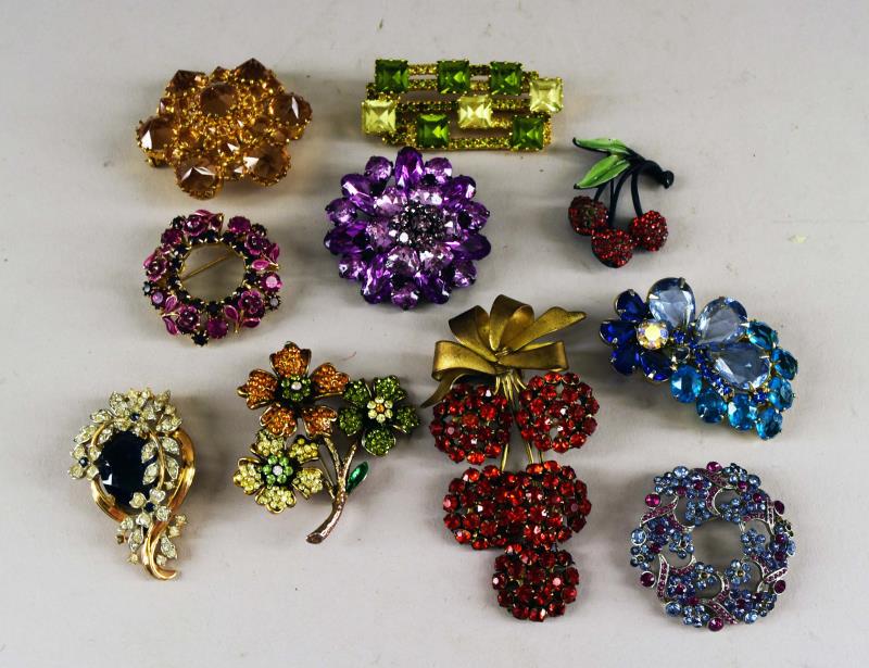 A Collection Of Vintage Pins: Consiting Of A Vintage Crown Trifari Rhinestone And Blue Center Stone Pin, A J J Cherry Pin (missing Some Rhinestones), An Austria Green Rhinestone Pin And Citrine Colored Pin, Four Purple, Pink And B