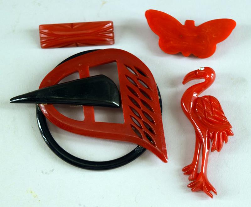 A Group Of Red And Black Bakelite Pins: Consisting Of Red Bakelite Stork And Butterfly Pins, A Red Bakelite Carved Pin And A Red And Black Bakelite Pin Made From Ribbon Buckles And Bracelet. The Large Pin Measures 3.75" Across. All Tested A