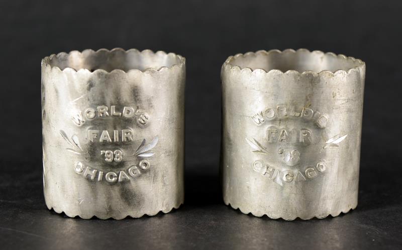 Two 1893 World's Fair Napkin Rings: Featuring A Pair Of Embossed Aluminum Napkin Rings With '93 World's Fair Chicago. Measuring1.75" Tall And 1.5" Across. One Has Significant Wear To The Embossed Chicago, Both Are Misshapen.