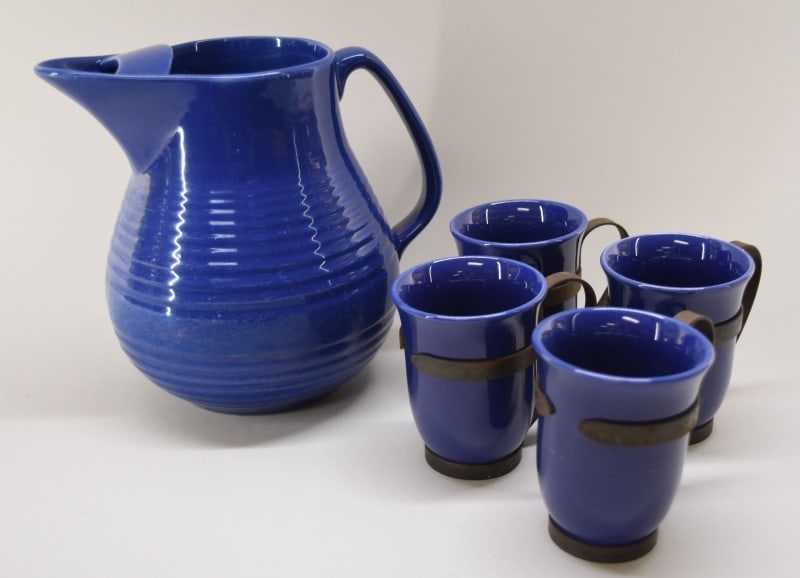 Bauer Pottery Cobalt Blue Pitcher And Cups: Featuring A Bauer Pottery Ring ware Pitcher And Four Mugs In Iron Holders. The Pitcher Measures 7 1/2" Tall And 7 1/2" Spout To Handle. The Mugs Measure 3 1/2" Tall And 2 1/4" Across The Top. All The